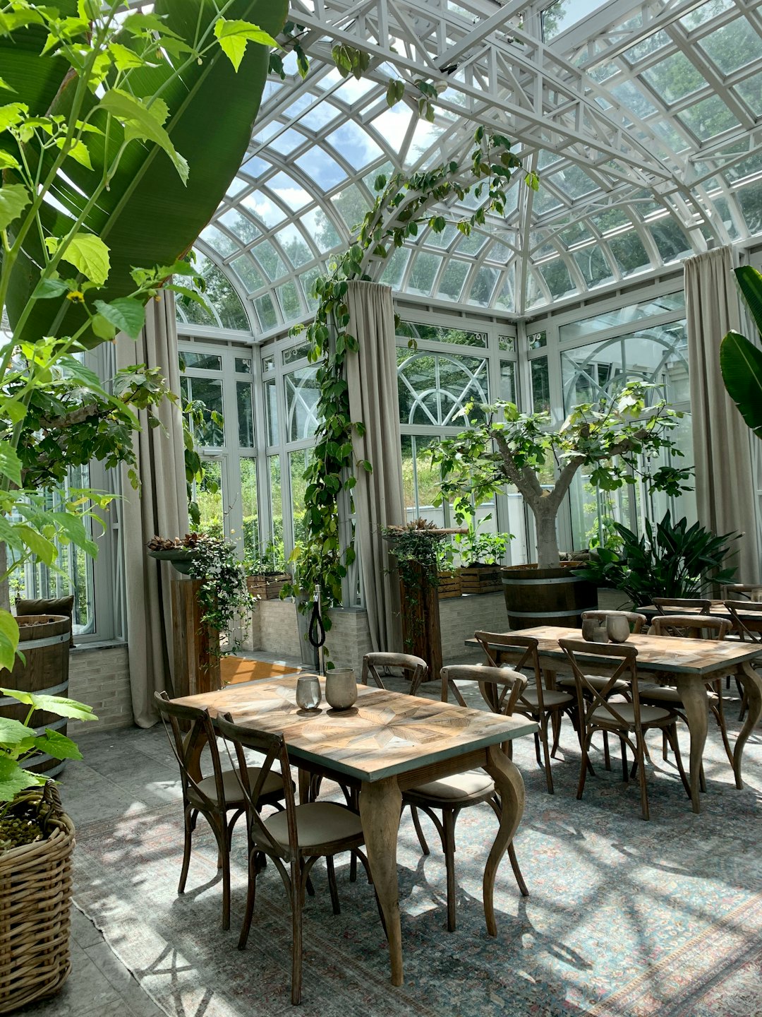 Zonnige serre met eethoek, planten en houten tafels.