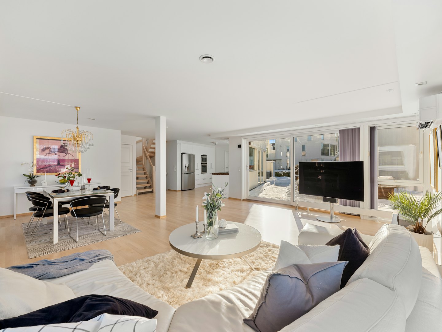 Moderne woon- en eetkamer met wit meubilair en houten vloeren.